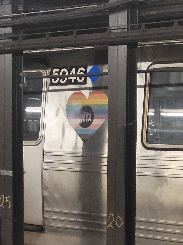 one of the subway trains at a new york subway station, with a heart in the pattern of an inclusive pride flag. cool!